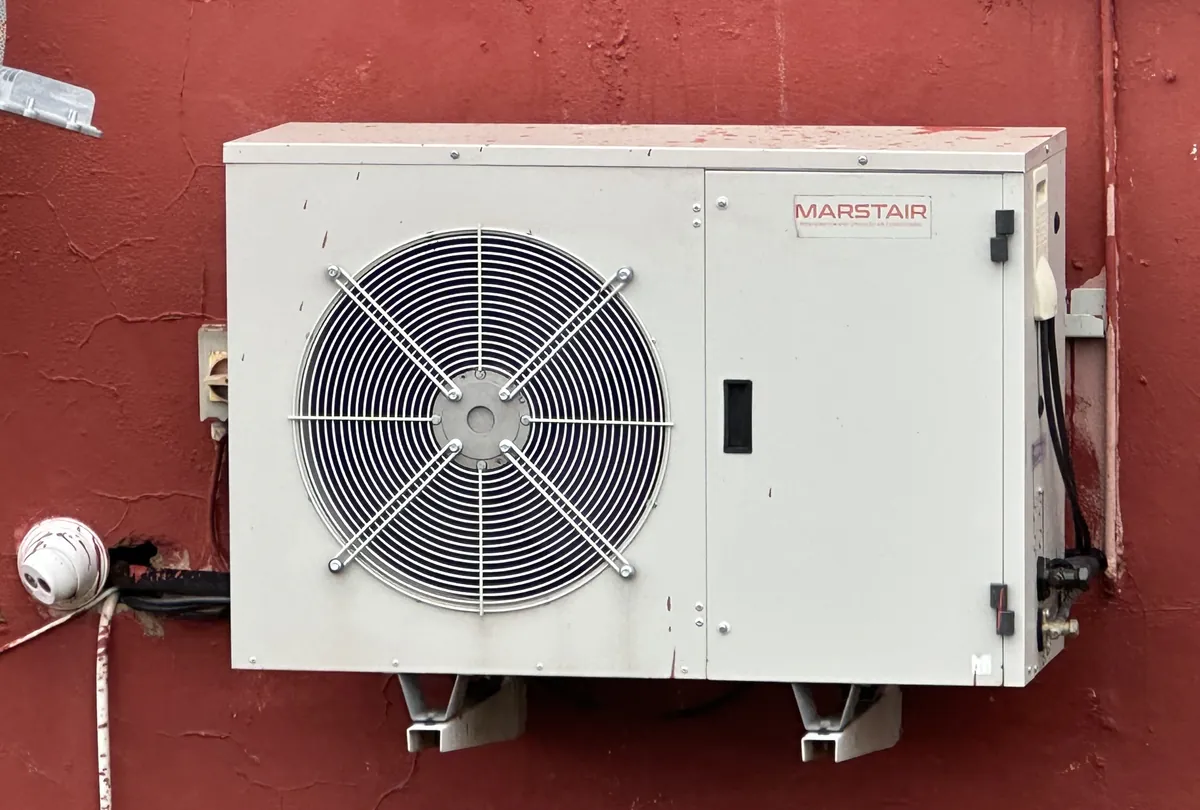 Unidad exterior de aire acondicionado montada en una pared, expuesta al ambiente costero